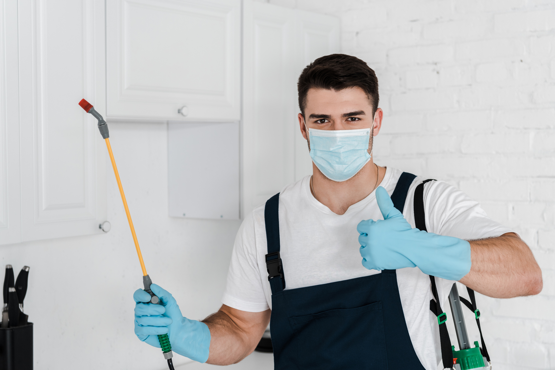 exterminator in uniform holding toxic spray and showing thumb up